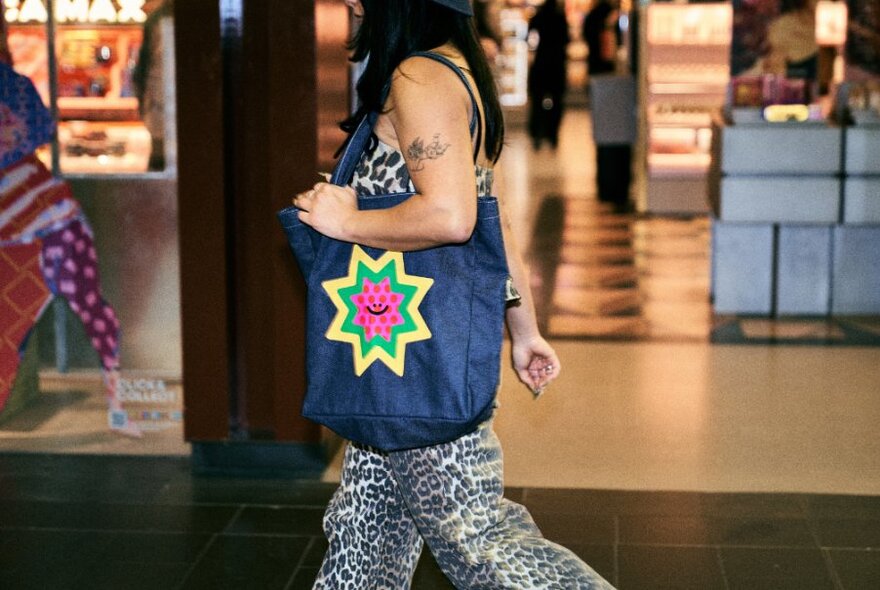 A person walking through Melbourne Central carrying a denim tote bag with a bright star pattern on it.