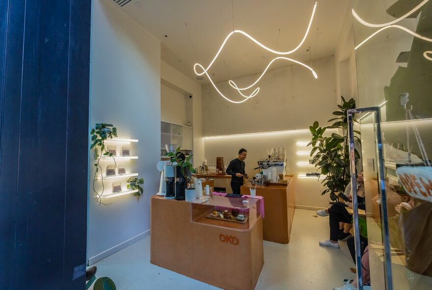 A barista in a small cafe with neon lights and plants.