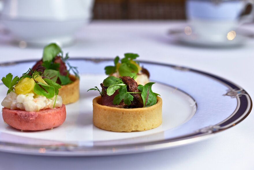 Small morsels of savoury food arranged on a white plate as part of a high tea.