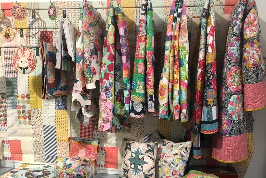 Hand-crafted quilts haning on rails in front of other quilted homewares.