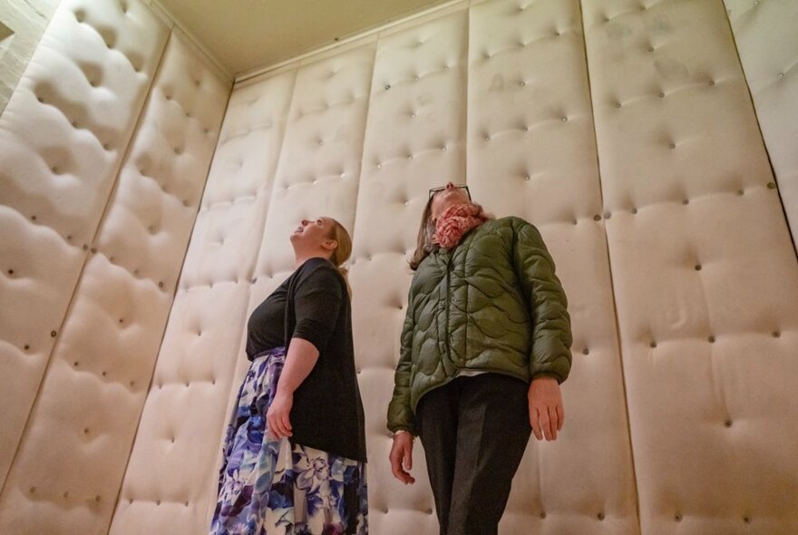 Two women staring upwards in a padded cell. 