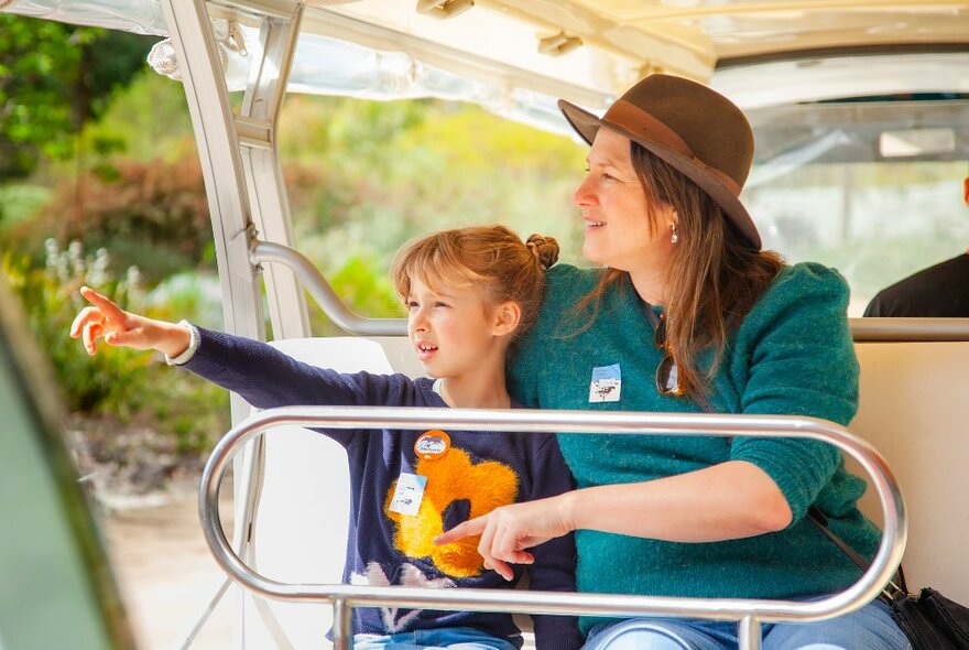 An adult and child riding in an open bus, the child pointing at something. 