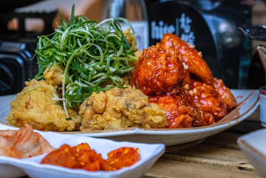A plate of Korean fried chicken, served  with condiments, on a wooden table in a restaurant.