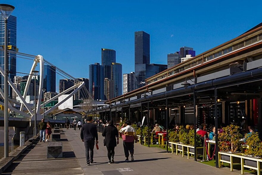 Riverside dining with three people walking along the promenade in Melbourne.