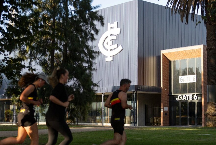 People running around Princes Park with the Carlton Football club rooms in the background.