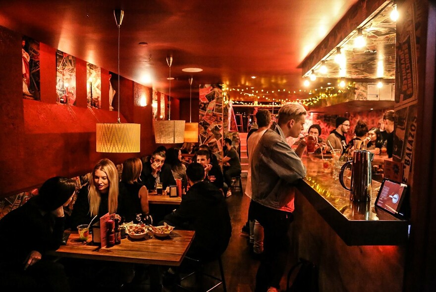 People standing at the bar or seated at small tables enjoying drinks and snacks.