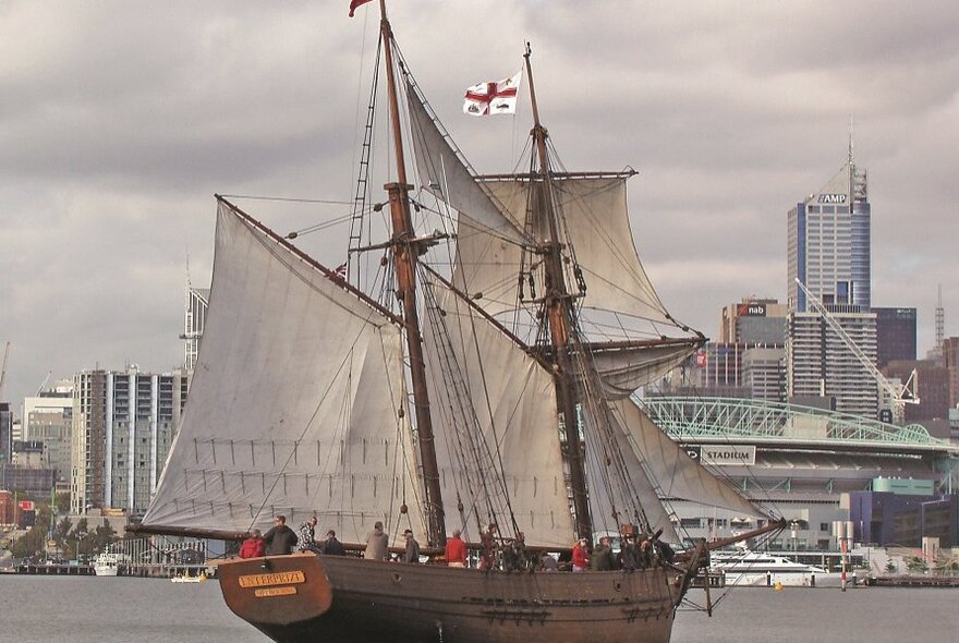 The 27-metre topsail schooner Enterprize a replica of a tall ship dating from 1830, sailing on water near Docklands, with Melbourne city buildings in the background.