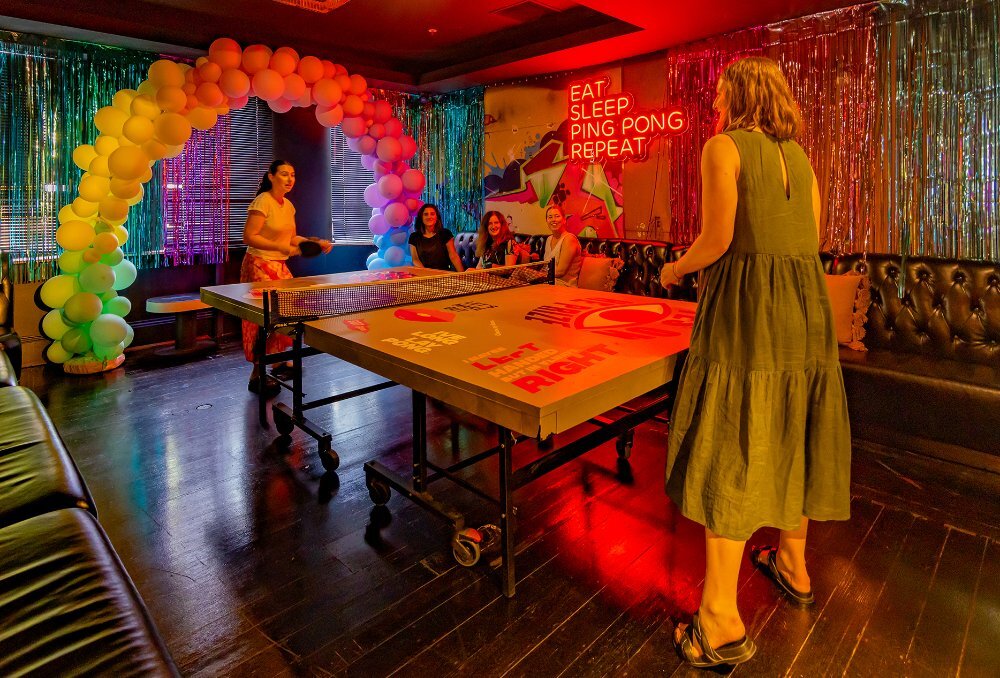 Two people playing table tennis while three friends watch on. 