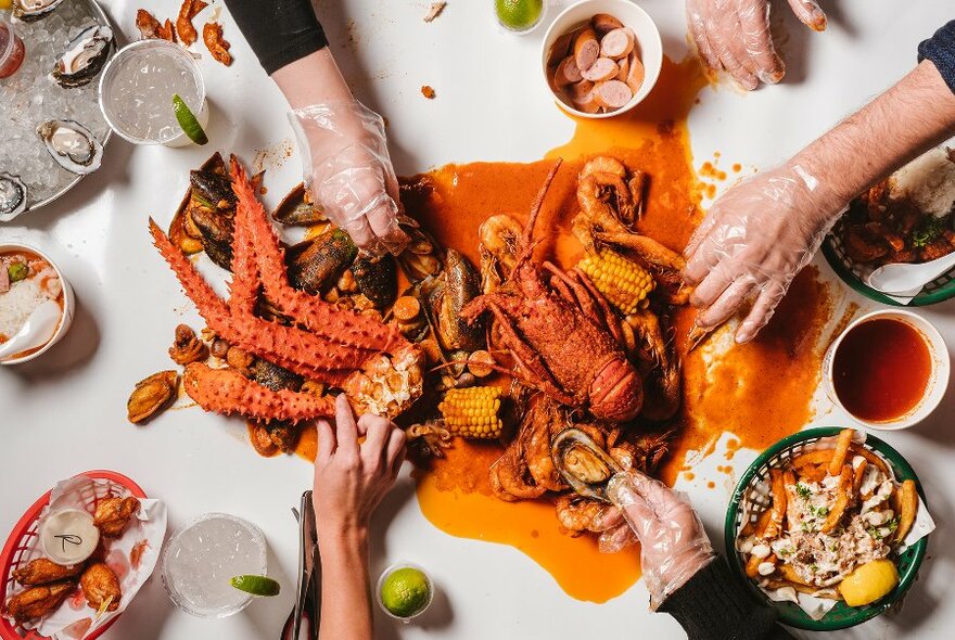 Hands grabbing bits of cooked red lobster on a white table.