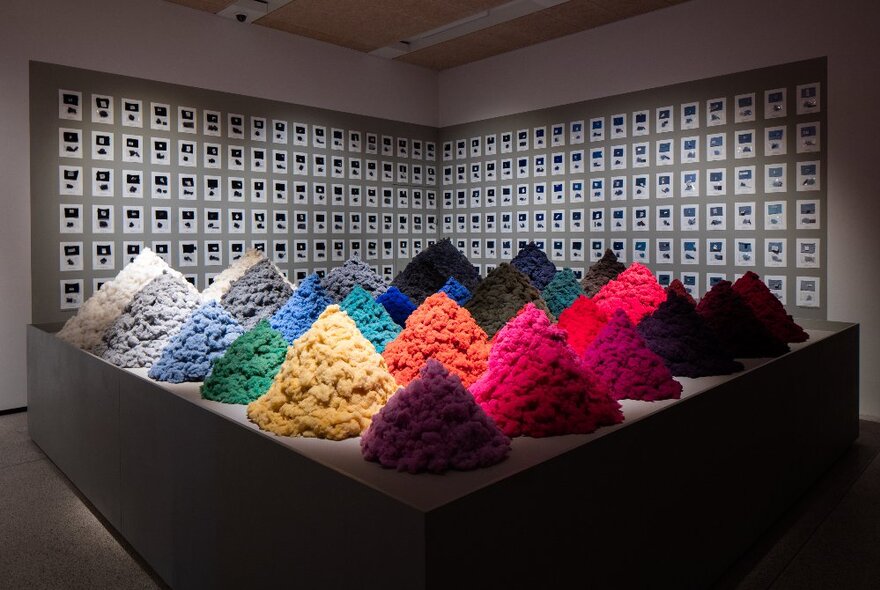 Triangular pyramids of brightly coloured woollen textiles on display in a gallery space.