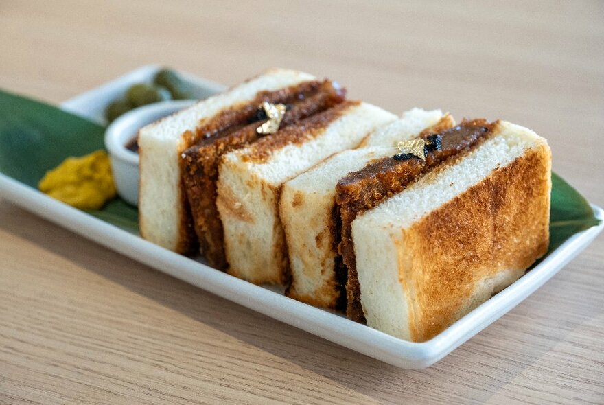 Close-up of a rectangular plate bearing two wedges of katsu sandos. 