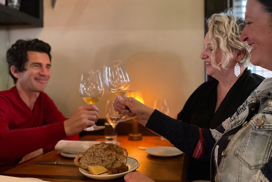 People clinking glasses at a lamplit restaurant table with a plate of bread and butter.