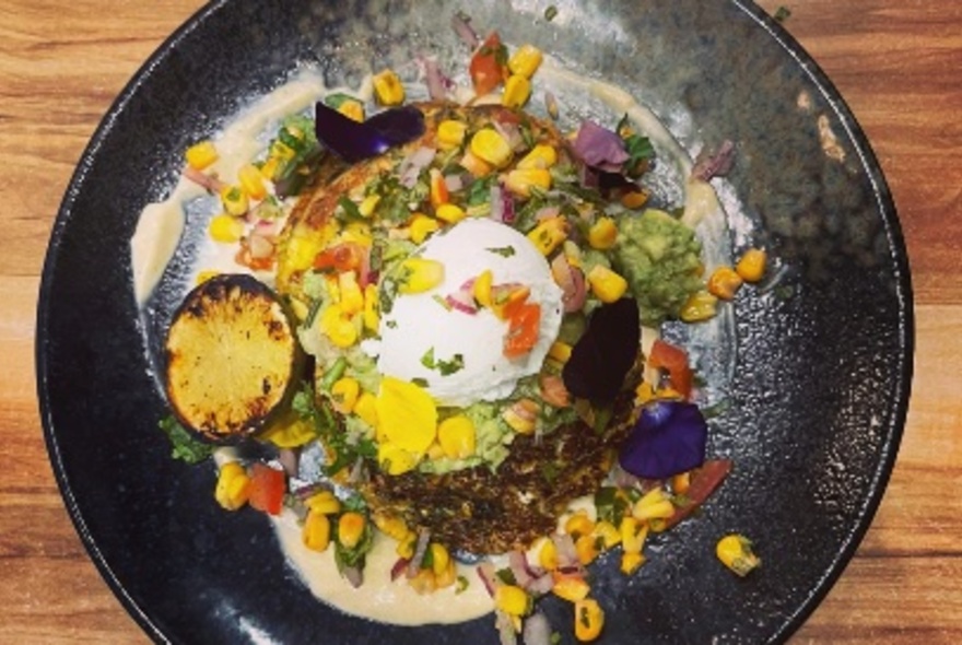 Overhead view of a plate of toast, poached eggs, sweet corn and other garnishes.