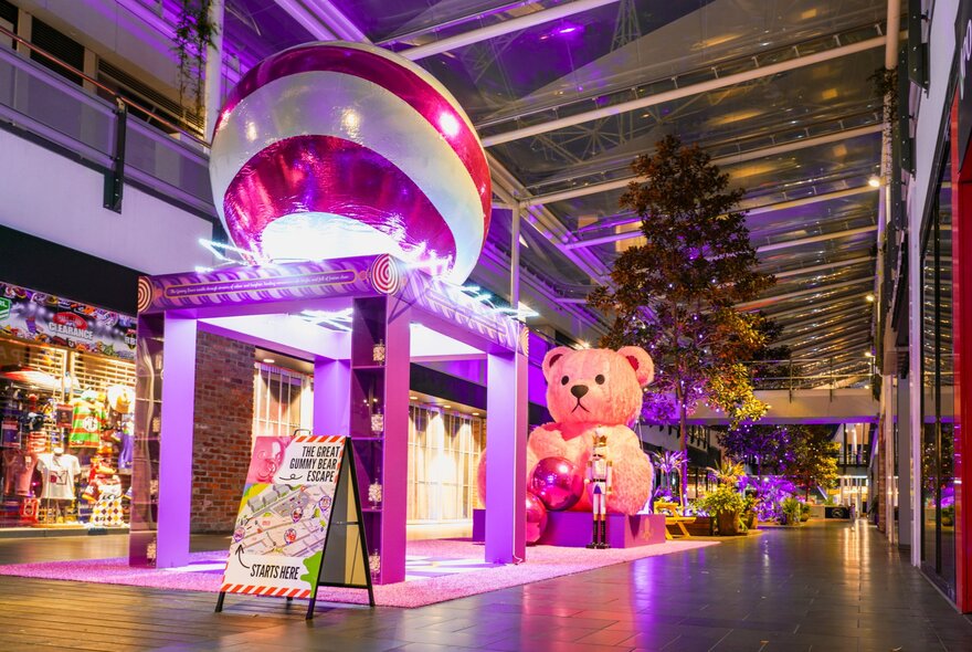 A large festive installation at District Docklands in the middle of the central walkway between the shops, with a giant teddy bear, Christmas tree and red and white Christmas bauble.