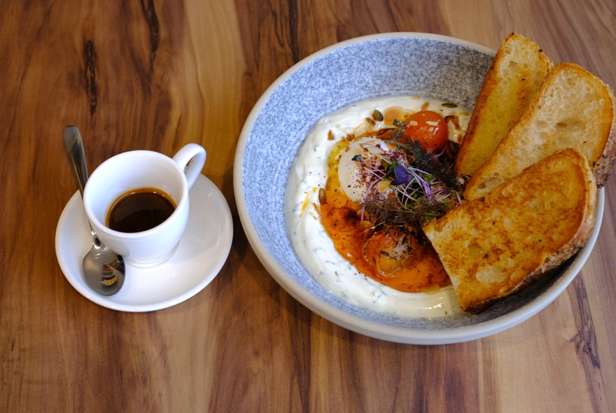 Poached eggs on a bed of creamy yoghurt, paired with toasted bread and a small ceramic cup of black coffee.