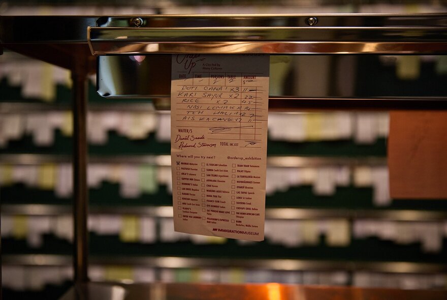 A service order docket hanging from the kitchen service area in a commercial kitchen.