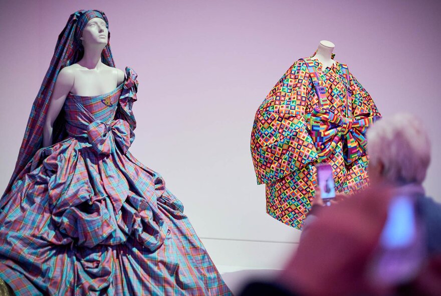 A person taking a photo of two mannequins dressed in colourful clothing in a fashion exhibition.