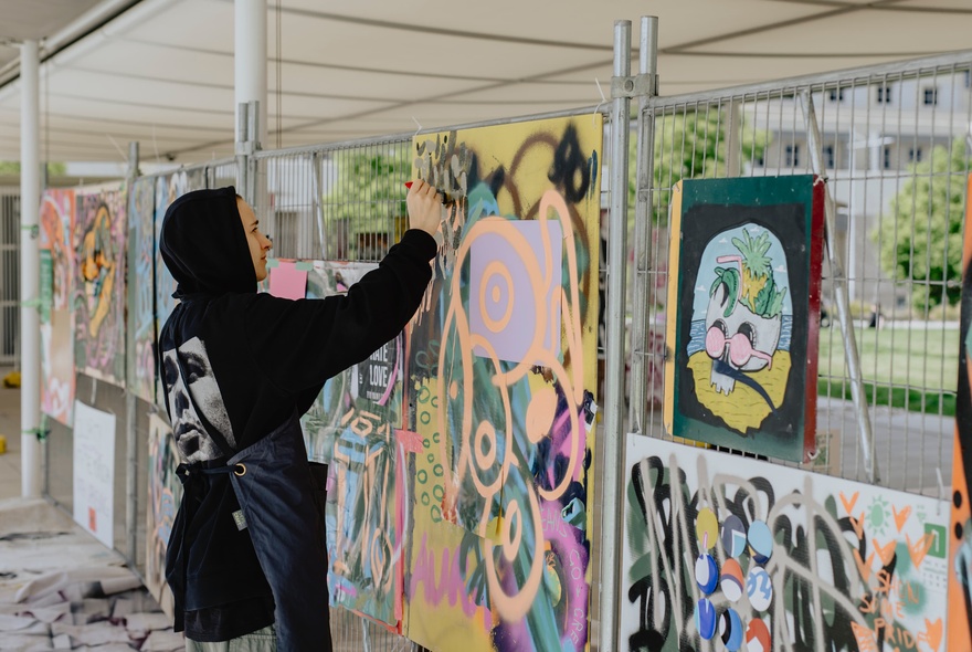 Person adding graffiti to an outdoor undercover walkway.