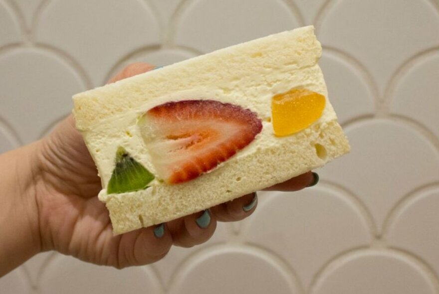 Hand holding fruity cream sando on it's side, showing inside filled with cream and fruit