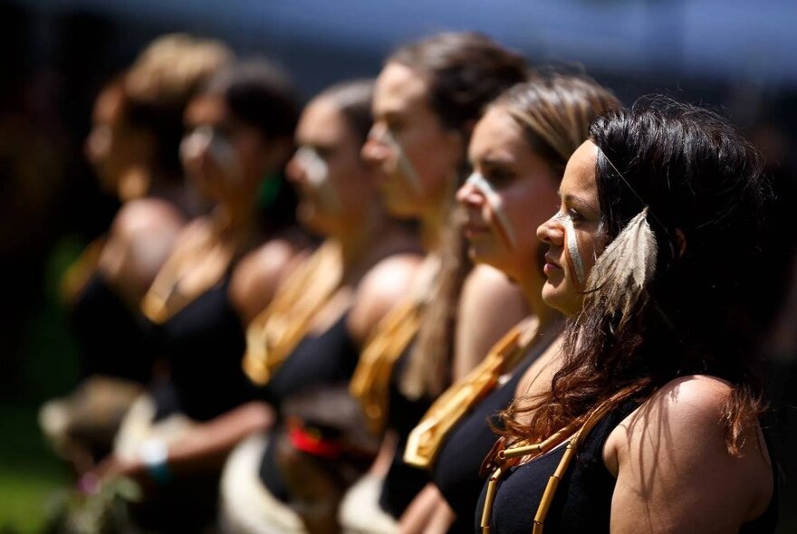 Six performers in profile in a line, all wearing black singlets, ready to dance.