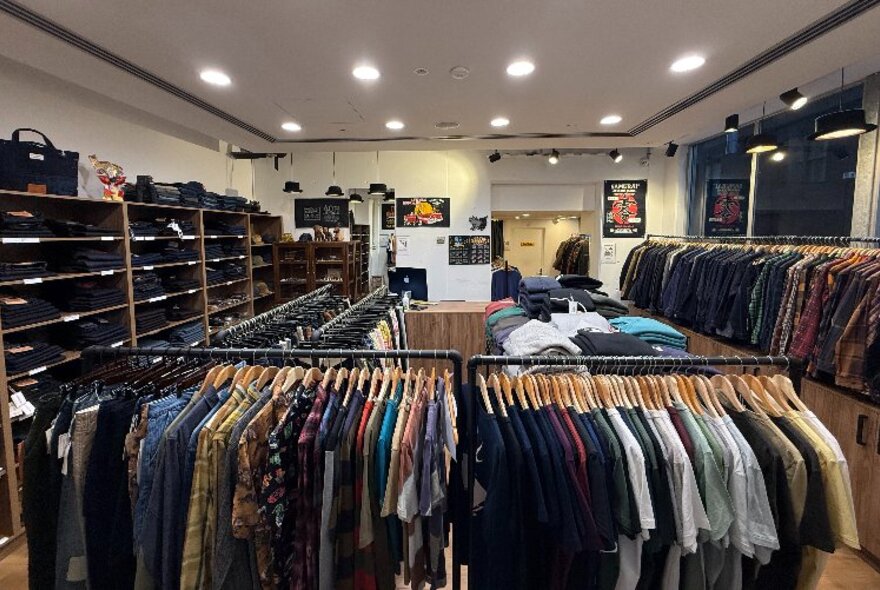 Interior of a retail store, with racks of clothes on display and a wall of shelves with folded denim jeans.
