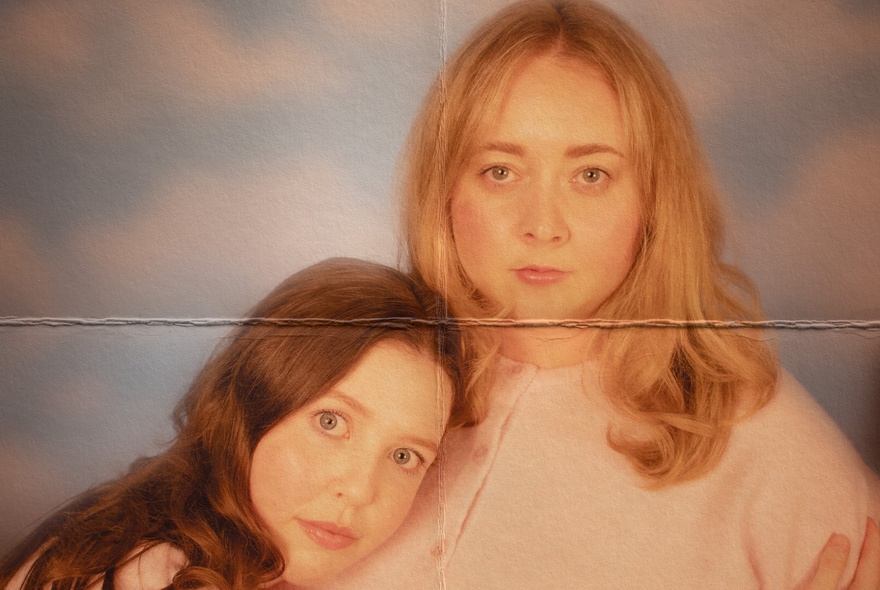 Faded picture of two women, one with her head on the other's chest, with a fold mark down the middle. 