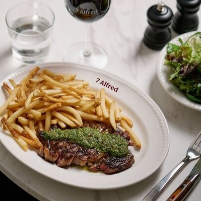 Steak frites with a chimichuri sauce on a white plate, accompanied by a green salad in a separate dish.