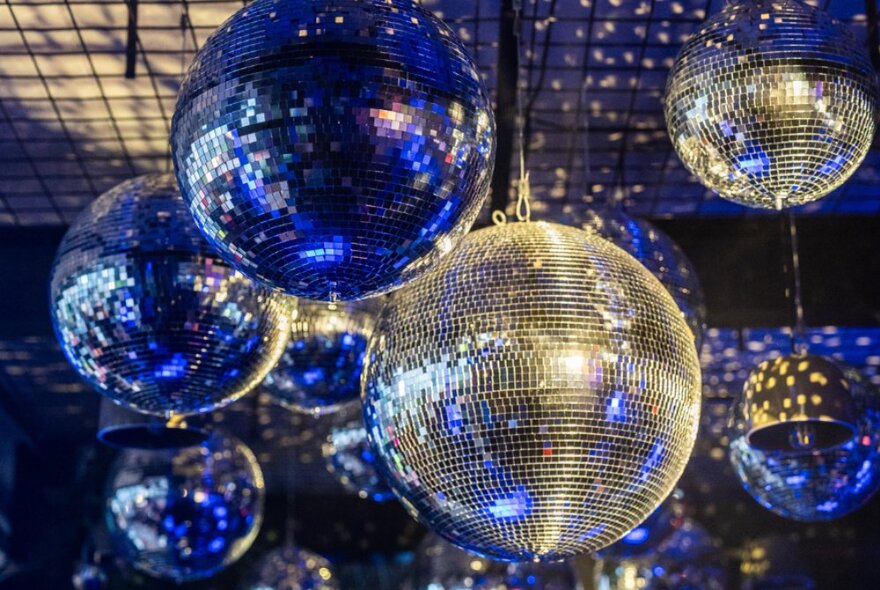 Several silver disco mirror balls hanging from the ceiling at an outdoor bar.