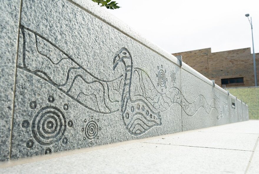 Indigenous artwork carved into the stone used in low fencing along a pathway.