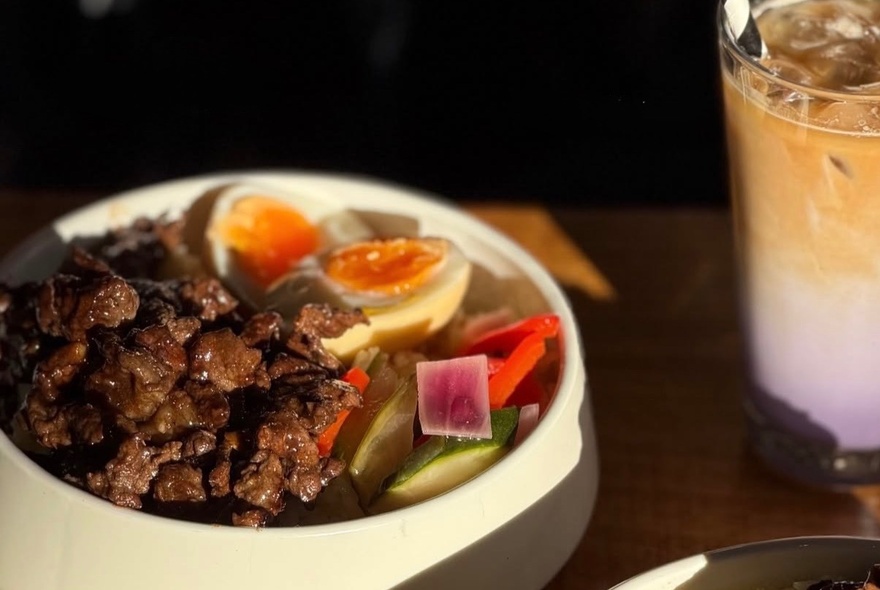 Dish of meat and vegetables with boiled egg next to a milky iced drink.