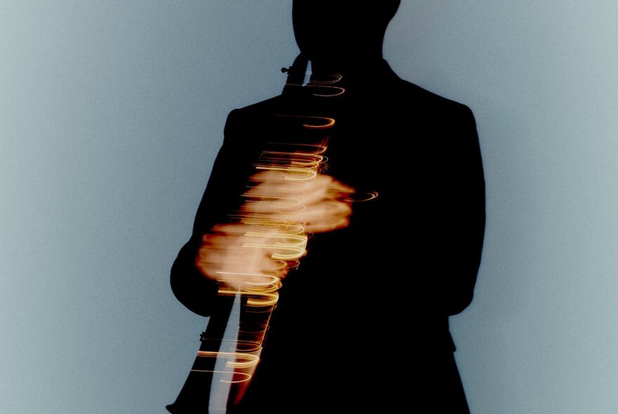 A dark silhouette of a person holding a clarinet that is blurred due to motion.