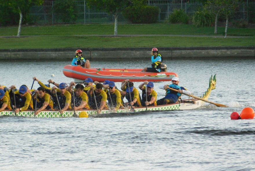 People participating in a dragon boat race with a rescue boat behind them.
