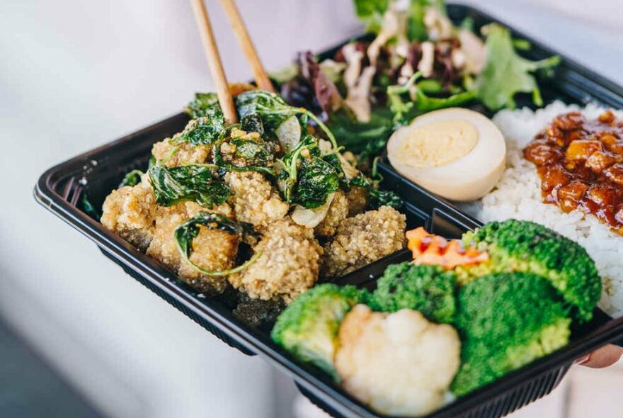 A bento box filled with fried chicken, garnished with crispy green herbs.