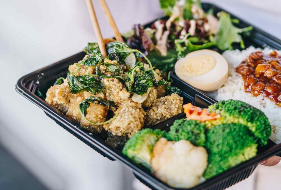 A bento box filled with fried chicken, garnished with crispy green herbs.