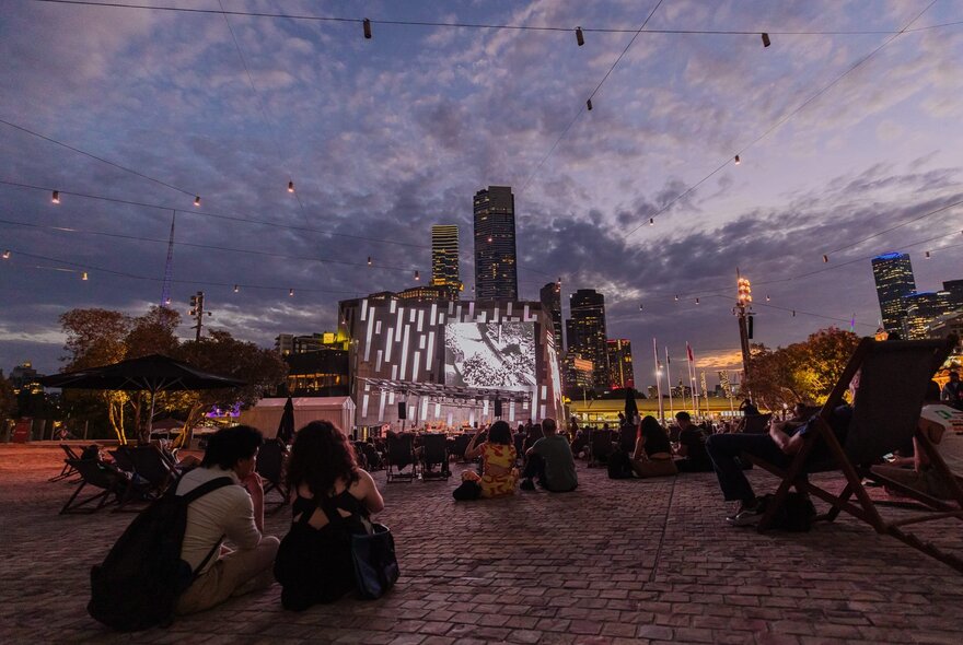 People seated on the ground watching an open air film screening at Melbourne's Fed Square.