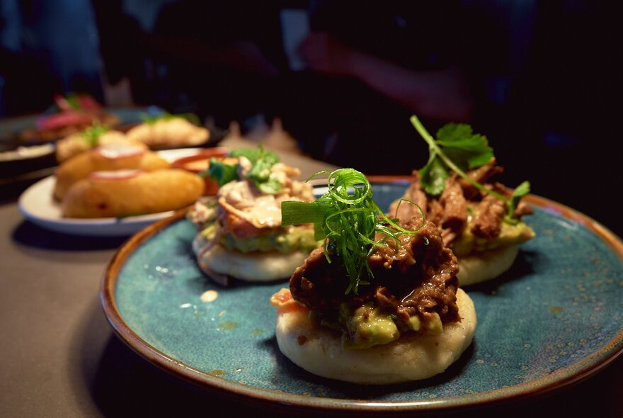 A plate of flattened bao buns with a meat topping, micro greens as a garnish.