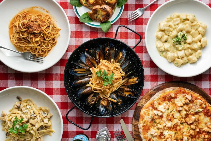 Overhead table display of pizza, and bowls of pasta and gnocchi.