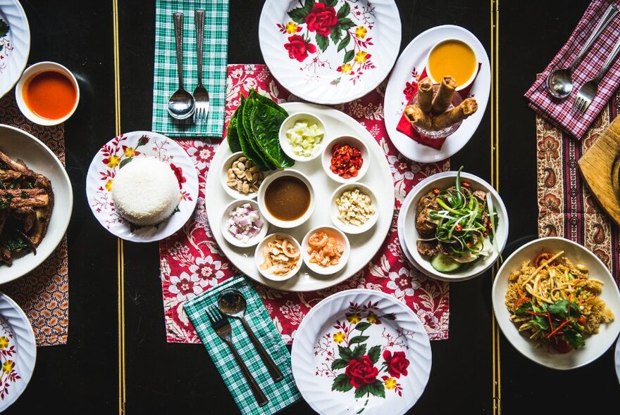 Overhead view of a table filled with plates of food of different colours and sizes, and colourful cloth checked napkins.