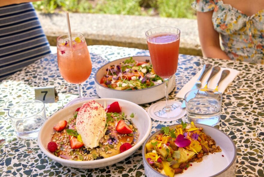 Speckled table topped with hotcakes, cocktails, and scrambled eggs.