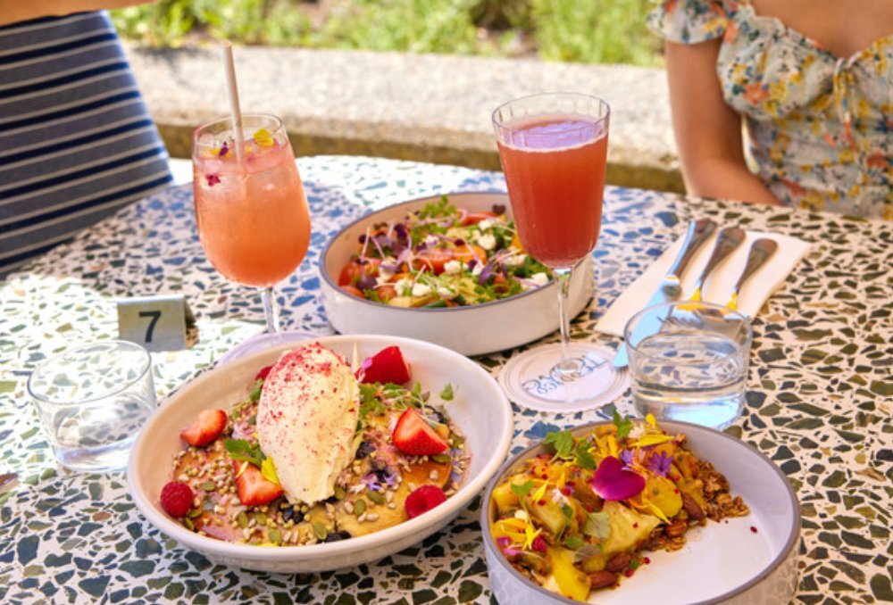 Speckled table topped with hotcakes, cocktails, and scrambled eggs.