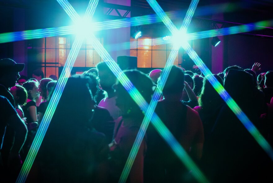 A crowd of people in a dark space at night, with the starbursts of two spotlights cutting through their silhouettes.