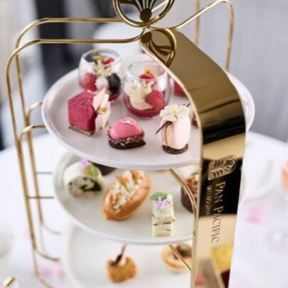 A three-tiered cake stand on a white table with pink champagne. 