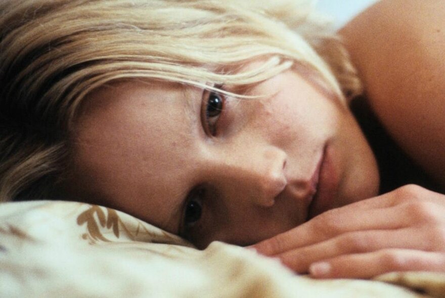 Blonde woman lying on a pillow, looking sad.