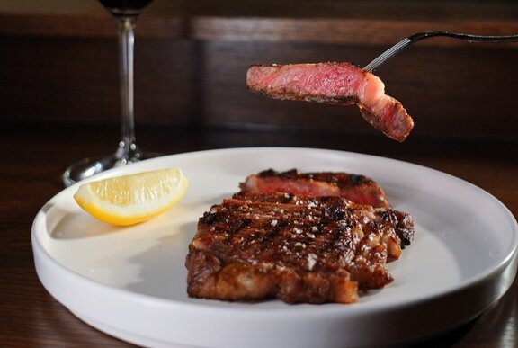 A wood-fired steak served on a white plate with a lemon wedge and sauce.