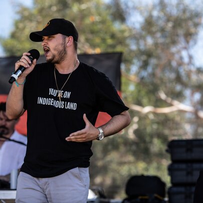 Singer wearing a T-shirt and cap, gesturing with his hand.