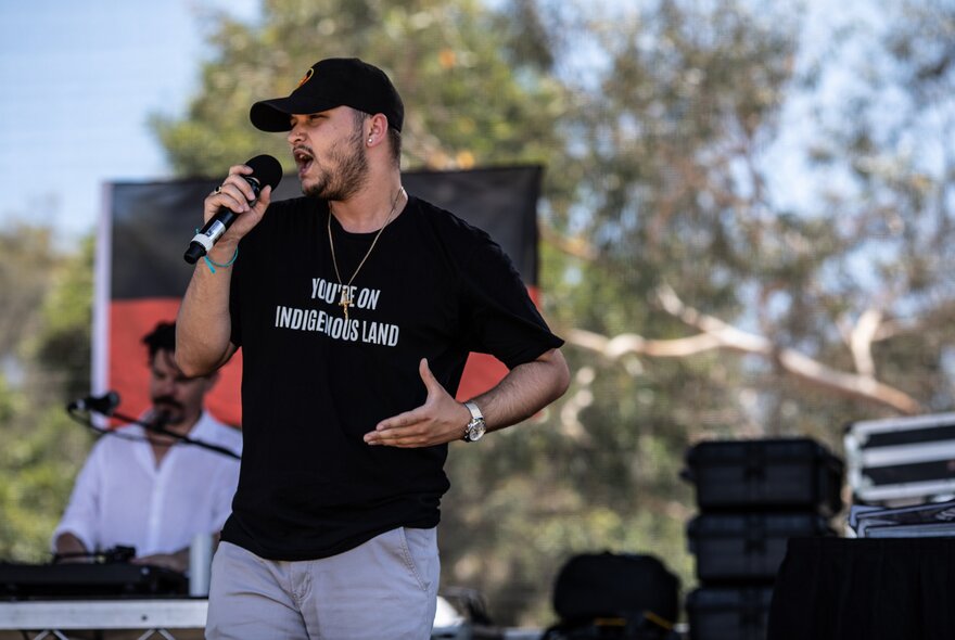Singer wearing a T-shirt and cap, gesturing with his hand.