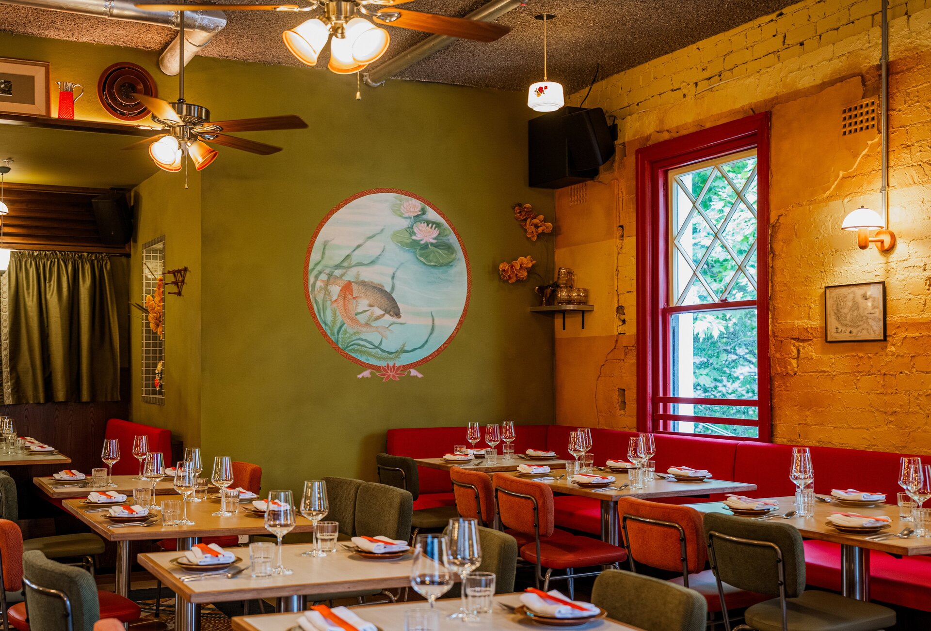The interior of a Southeast Asian restaurant with red and green decor and a painted mural on the wall.