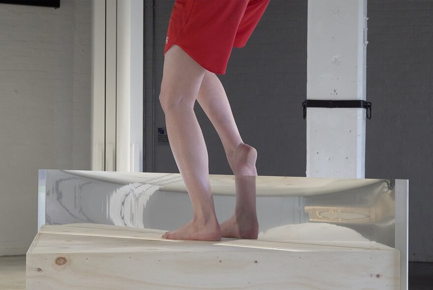 Legs reflected in a mirrored rectangular block as part of a performance piece.