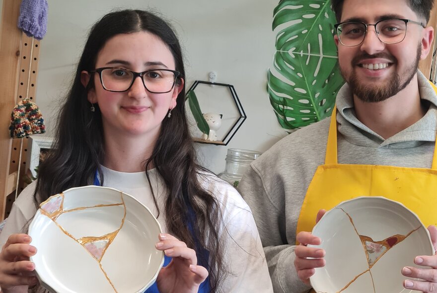 People holding broken plates mended with gold glue and mismatched patterned inset.