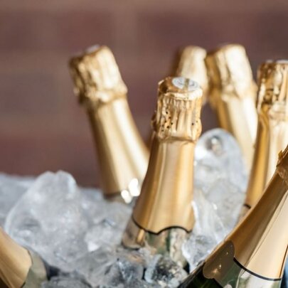 A close up photograph of the gold foil-covered tops of seven champagne bottles resting in ice.